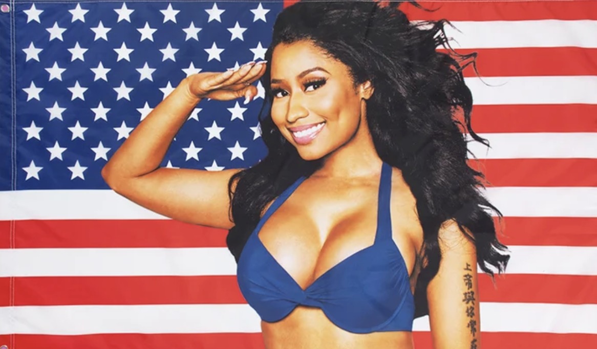 Nicki Minaj saluting and smiling in front of an American flag